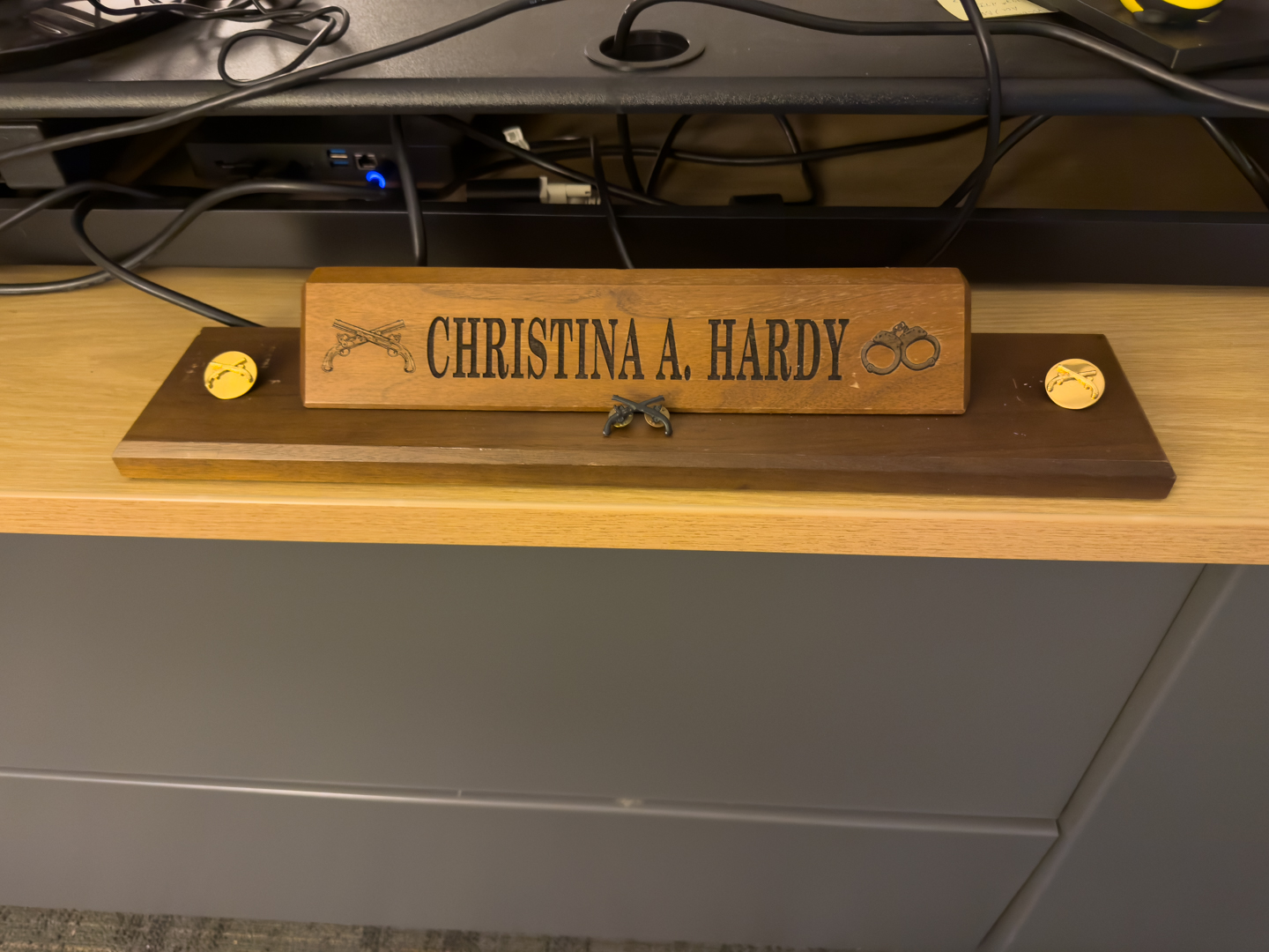 Original desk nameplate A nameplate on a wooden desk plaque with a decorative metal emblem.
