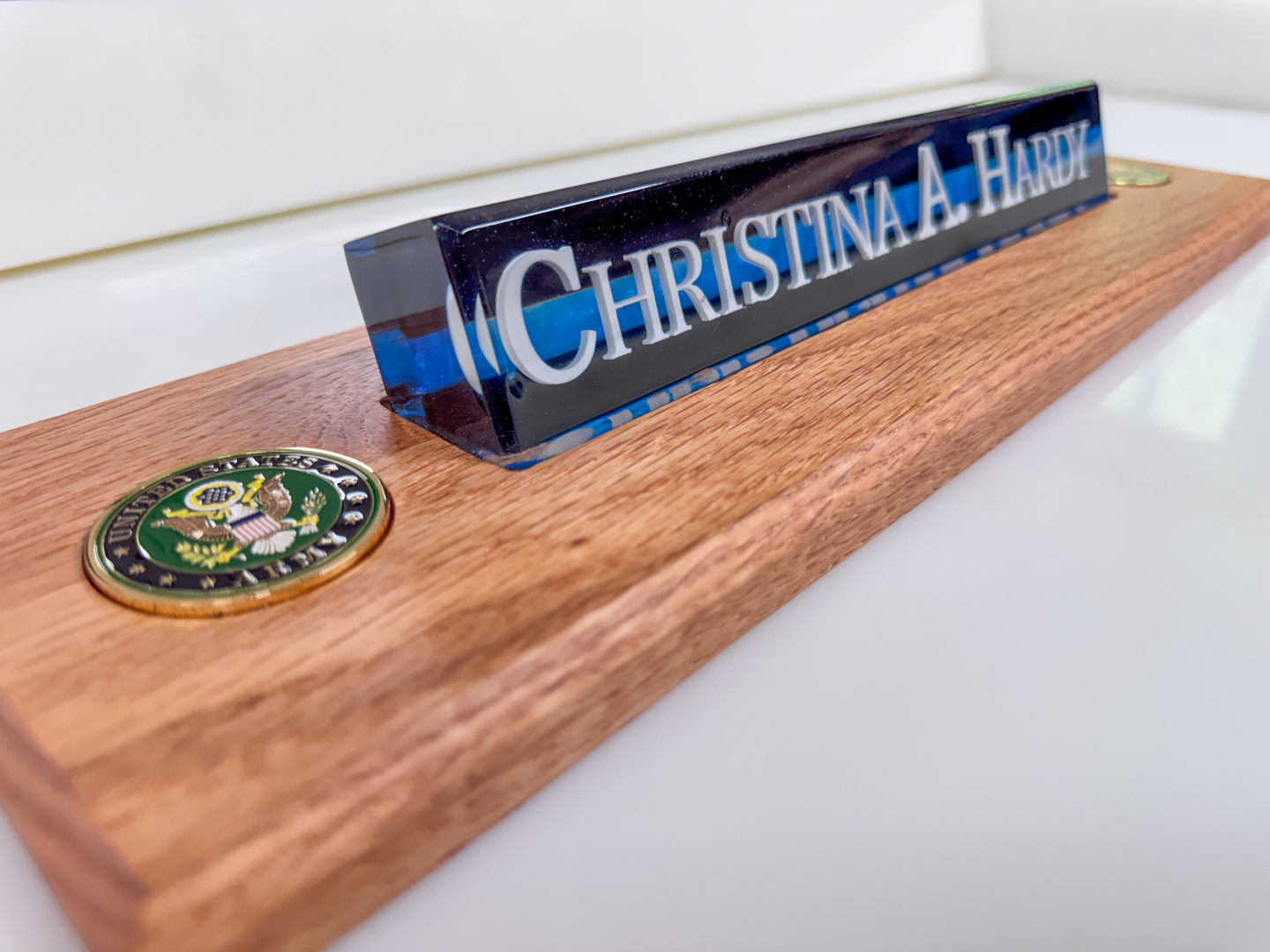 Personalized epoxy resin desk nameplate on wooden plaque A glossy custom epoxy resin nameplate sits on a wooden desk plaque with a decorative metal emblem.