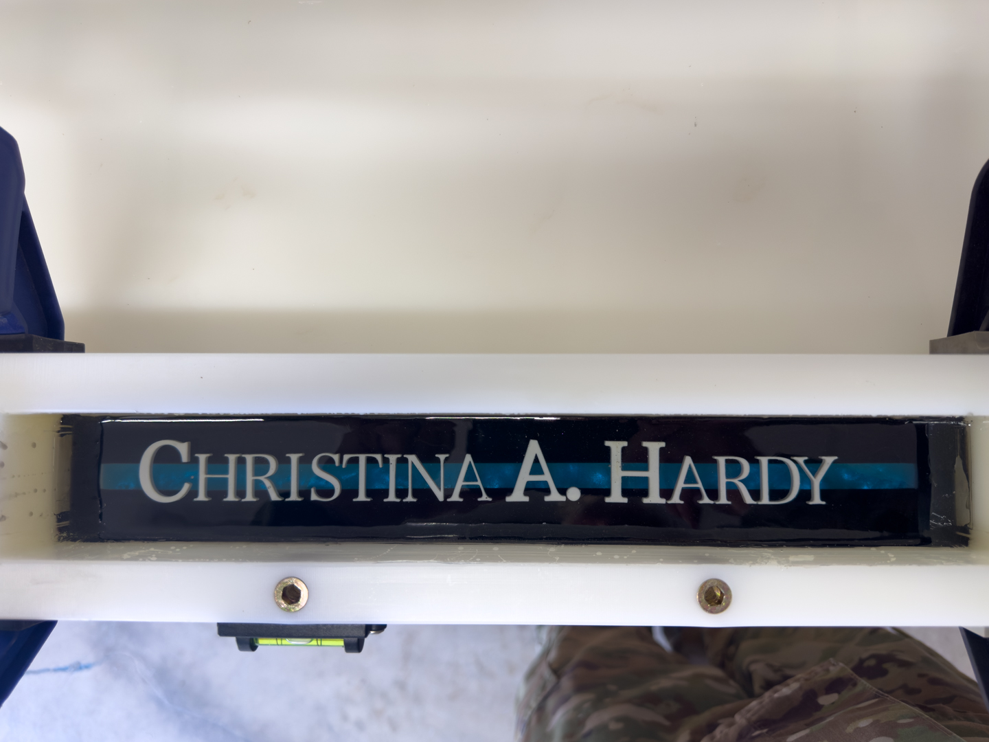 Personalized epoxy nameplate mounted on a white frame A custom nameplate with white lettering is mounted on a white equipment frame with visible hardware.