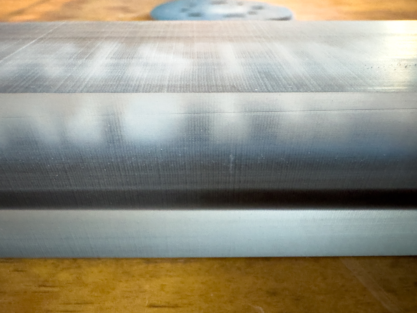 Close-up of a finished metal-look epoxy nameplate A close-up shows a blank rectangular epoxy or resin nameplate resting on a wooden work surface.