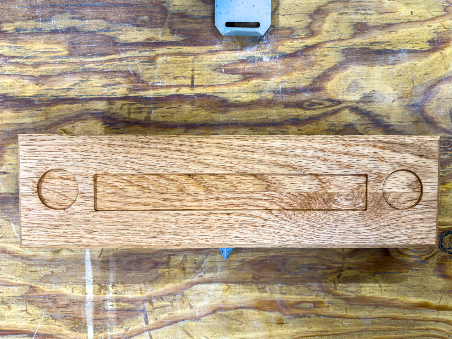An oak nameplate base with recesses for a resin block and two coins, on a workshop bench