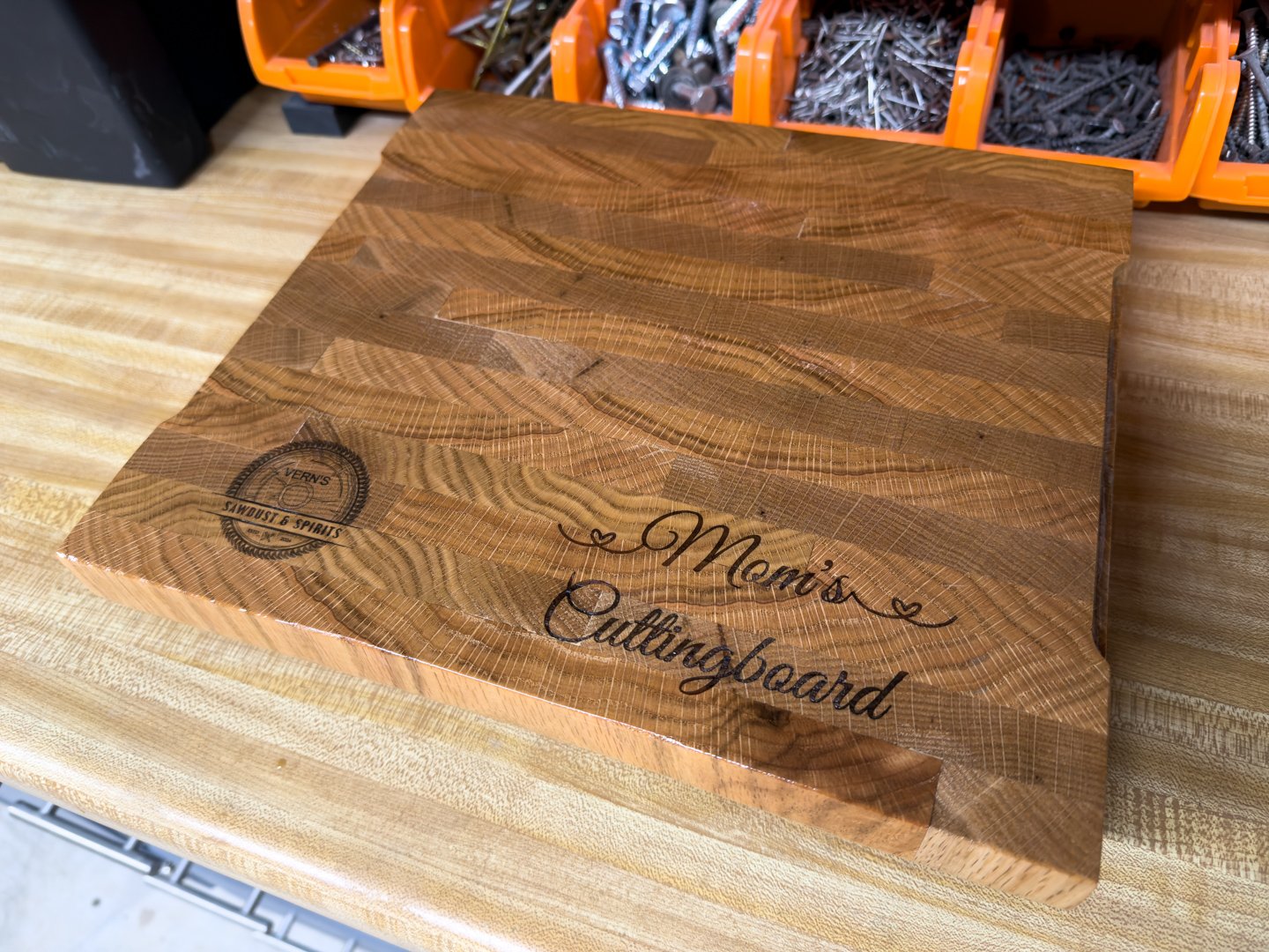 A custom engraved hardwood cutting board with a routed juice groove, resting on a workshop bench