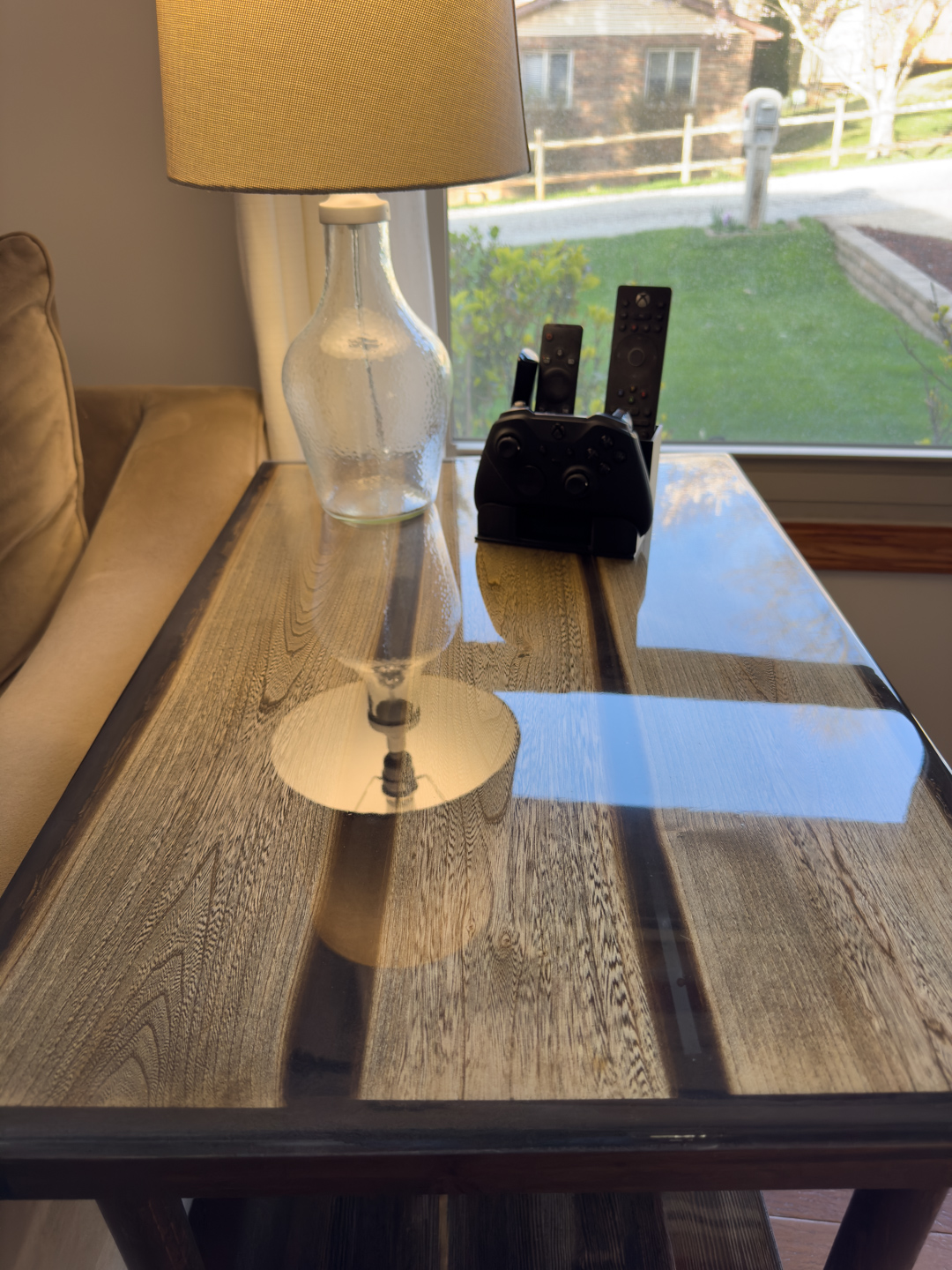 Handcrafted epoxy wood table by a window A handcrafted epoxy wood side table sits beside a lamp and remote controls in a bright living room.