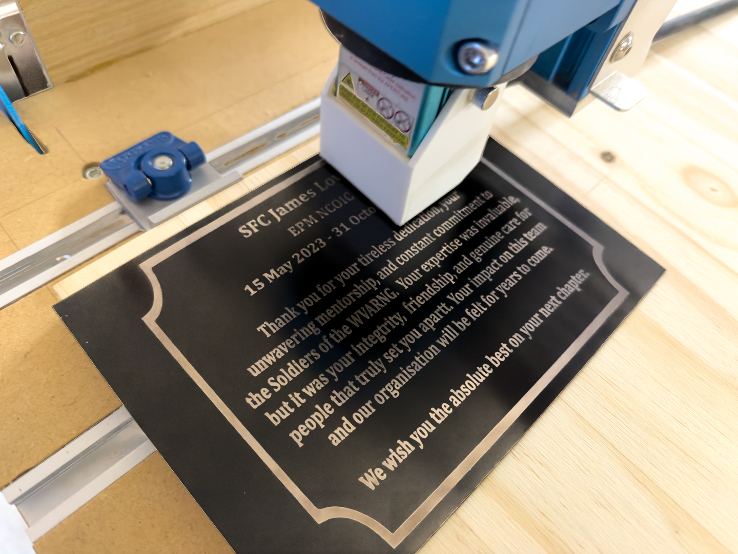 Close-up of a laser engraver etching a commemorative plaque A laser engraving machine is marking a black plaque on a wooden work surface.