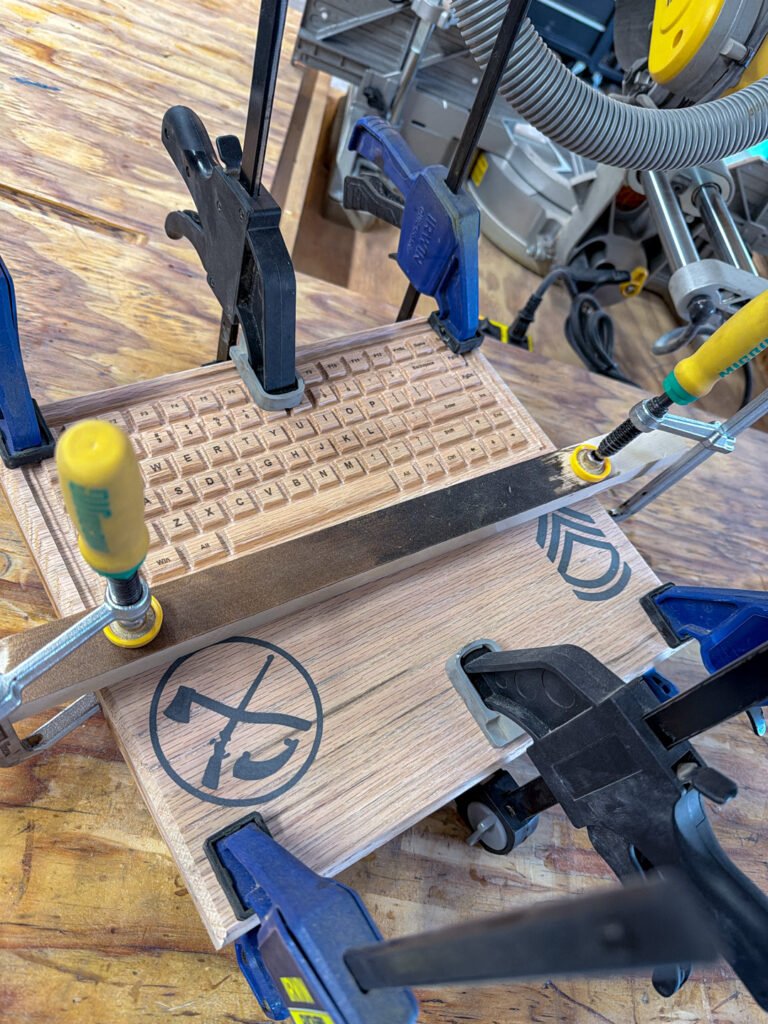 The wooden keyboard panel held in place with clamps on a workshop workbench.
