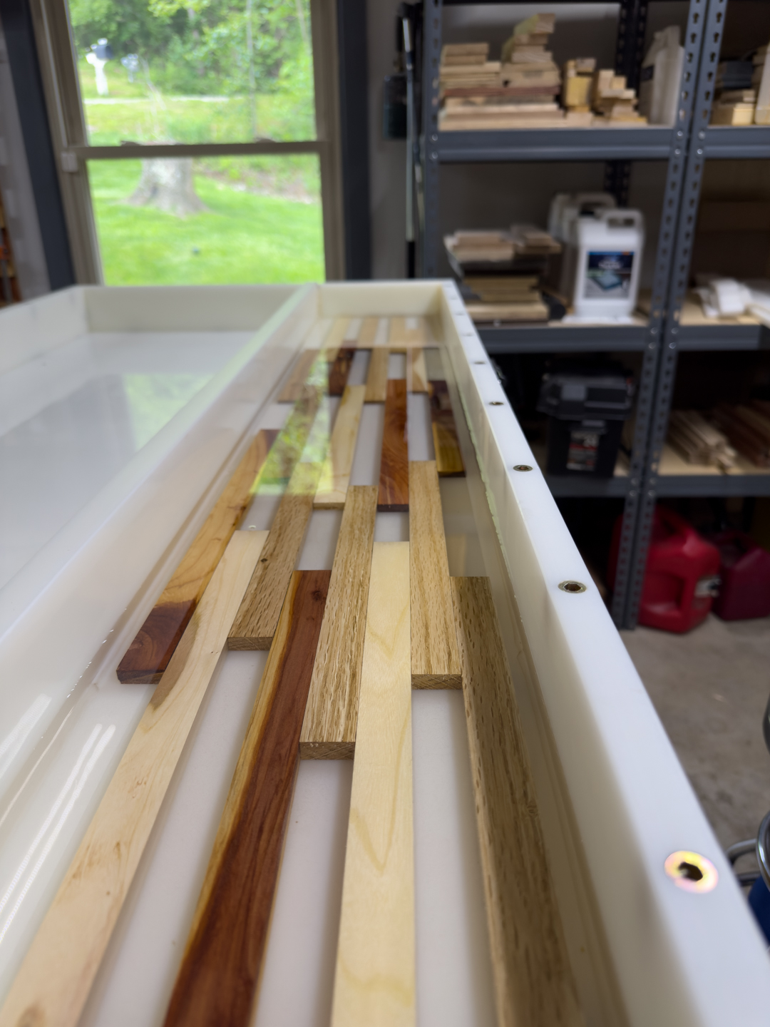 Wood strips of several kinds laid out in a workshop, with lumber racks in the background