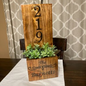 Stained pine planter box with a tall backboard carved with a house number and a script family name