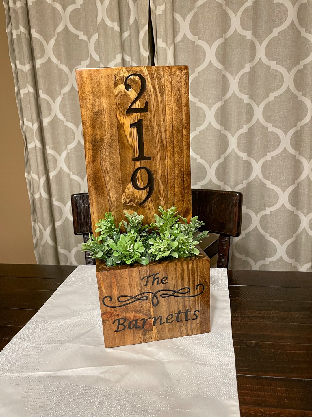 Stained pine planter box with a tall backboard carved with a house number and a script family name