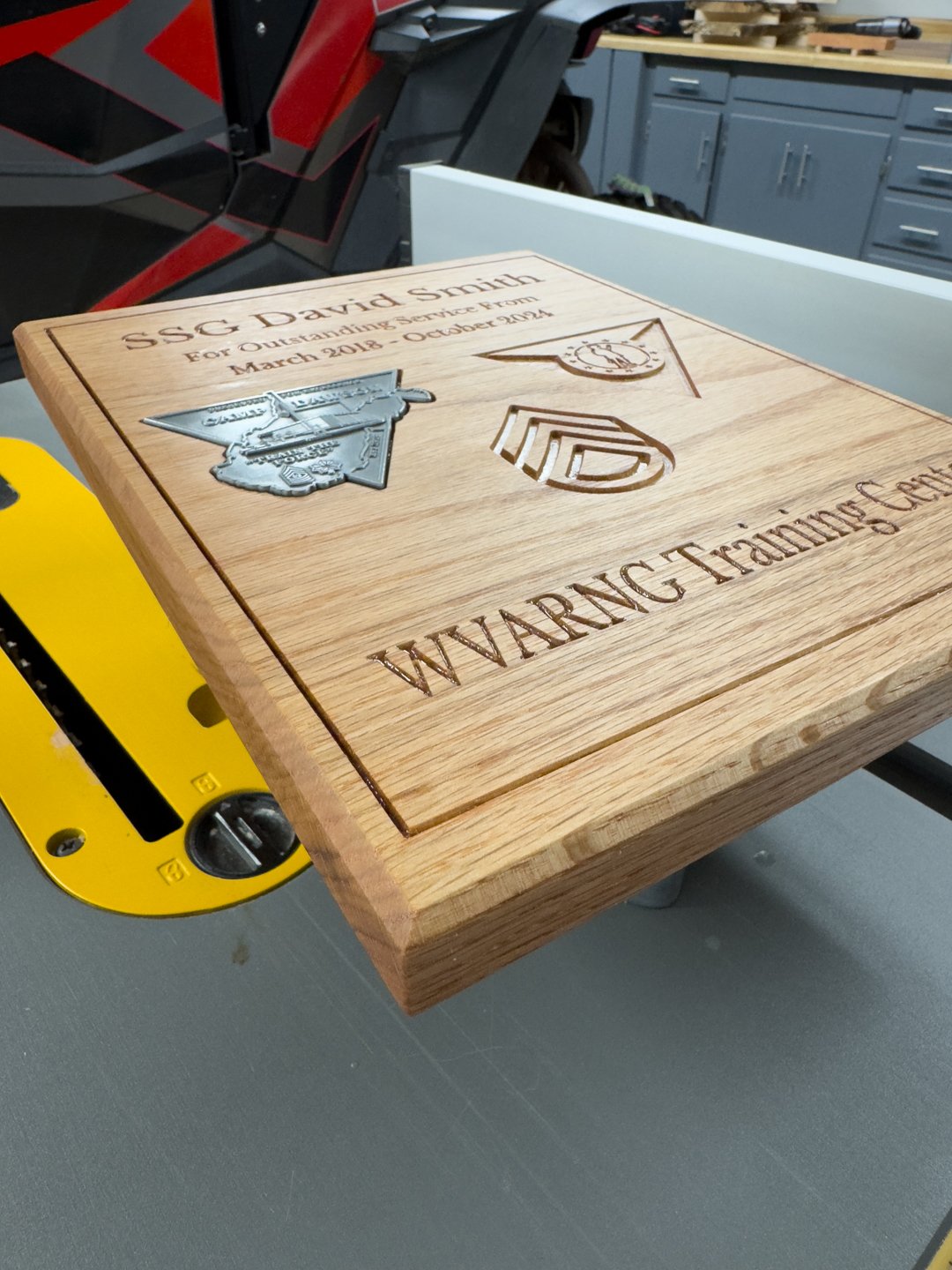 Oak service plaque engraved with a name, service dates, and unit emblem, on a workbench