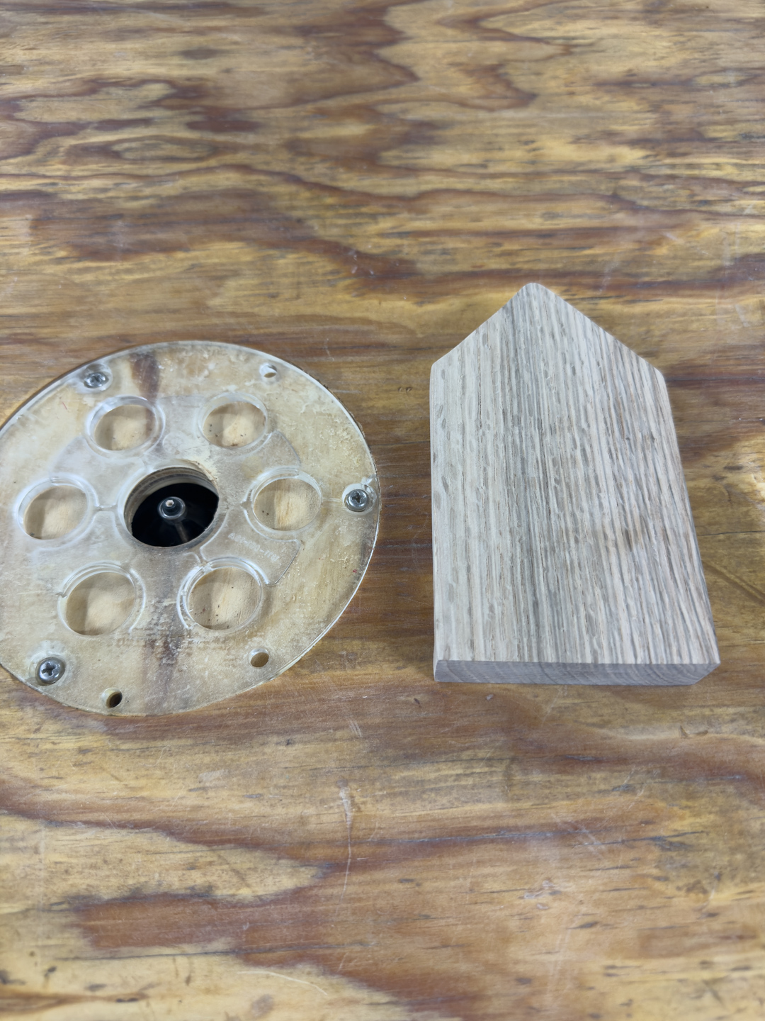 A router table with a wooden template guide next to a block of end-grain wood that has been cut with it