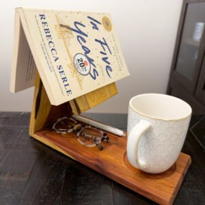 Personalized cedar reading holder on a sofa arm with an open book, mug, glasses, and pen