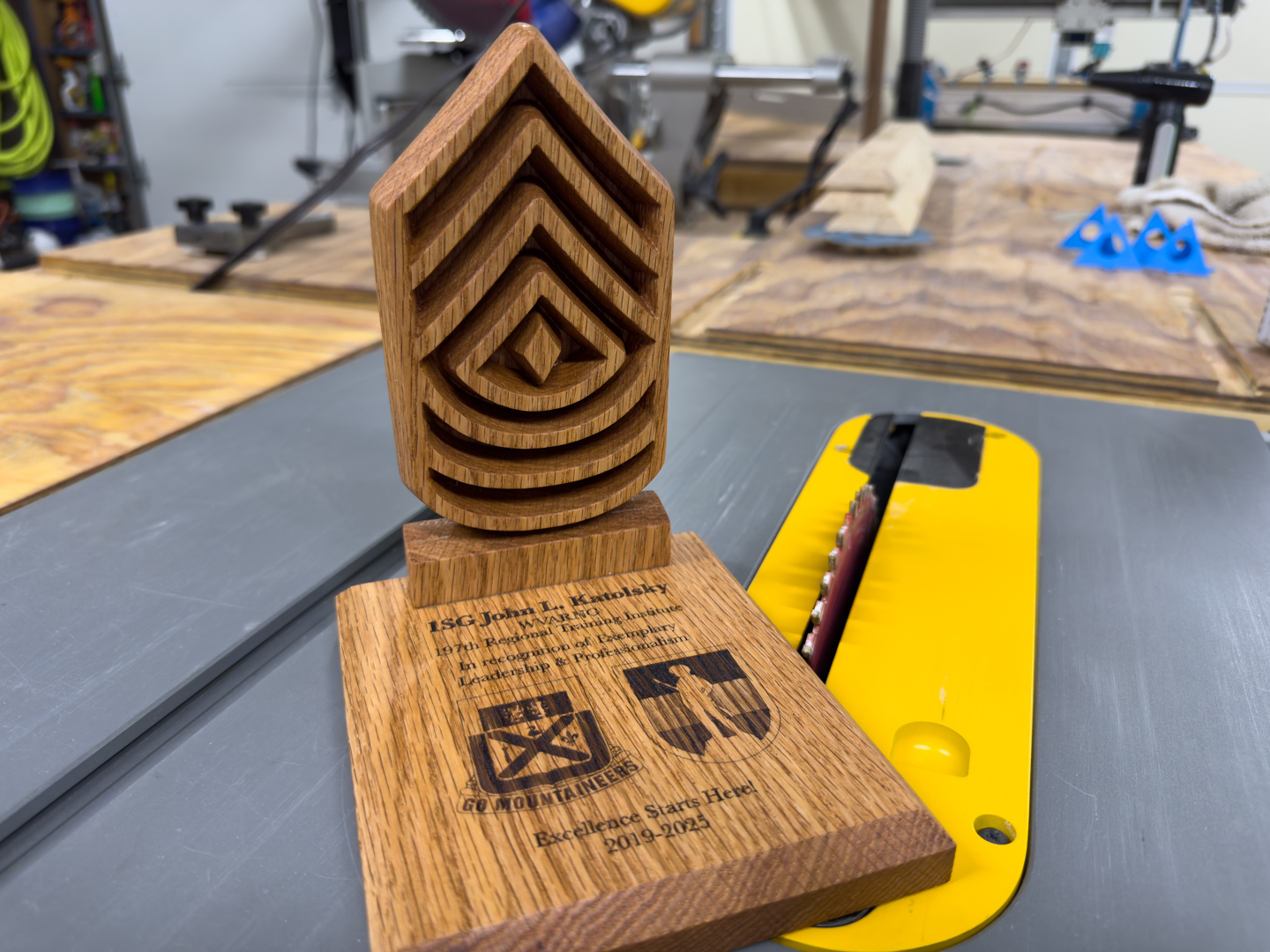 A wooden award trophy with three carved chevrons on an engraved base, standing on a shop table