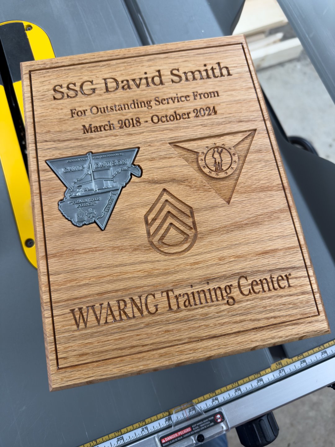 A wooden award plaque with a raised engraved emblem and rank insignia, on a workshop table