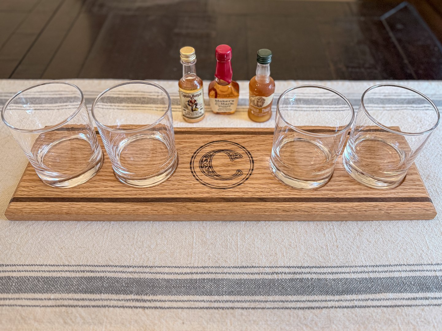 Oak whiskey flight board with a dark accent stripe, engraved monogram, and four glasses
