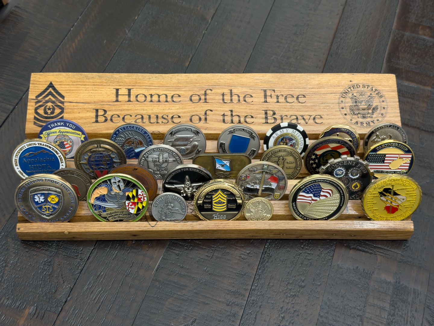 Wooden challenge coin display rack with a backboard reading Home of the Free Because of the Brave, holding many coins