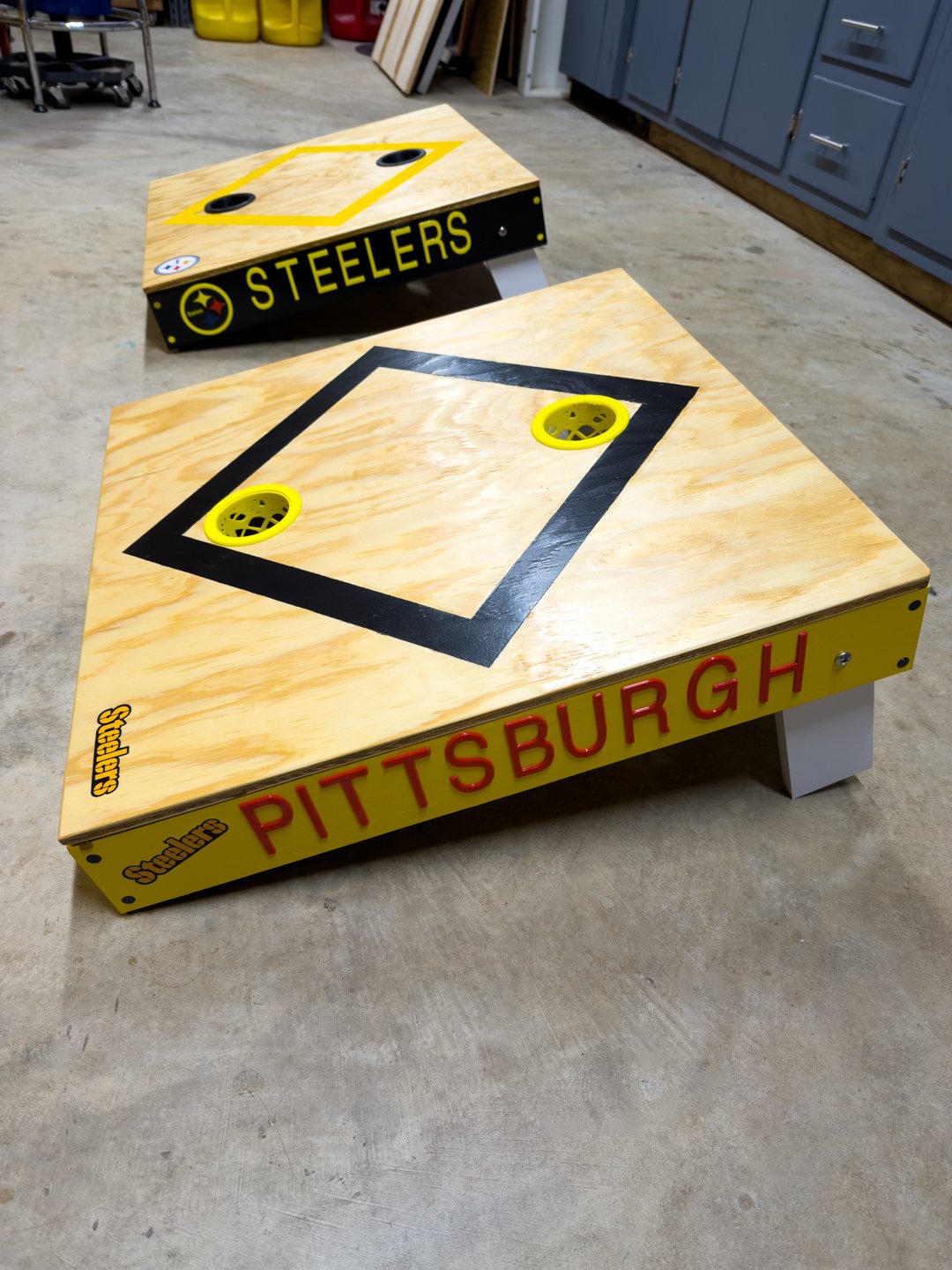 Two custom toss game boards with lettered side rails and painted diamond targets on the playing surface.