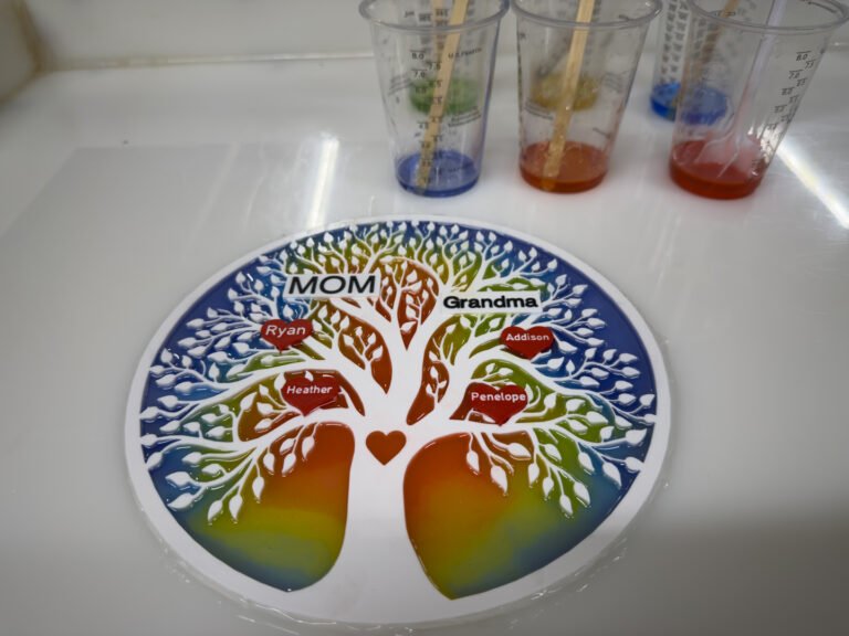 The tree of life on a white mat beside cups of tinted resin.
