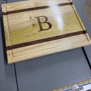 Monogram inlay cutting board with contrasting stripes and a large inlaid initial on a table saw