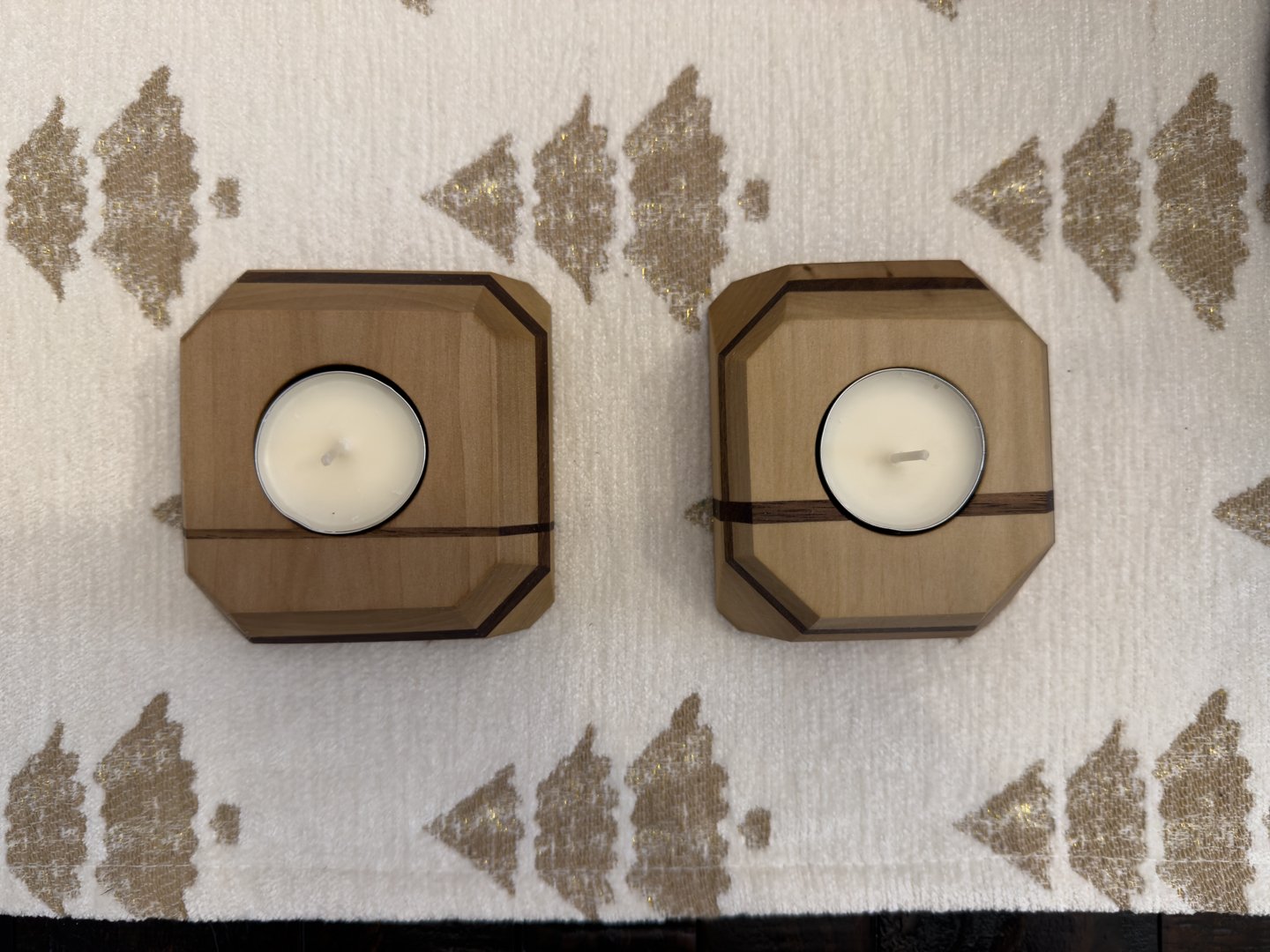 Two faceted hardwood tea light holders with a walnut stripe on patterned fabric, showing the chamfered top edges