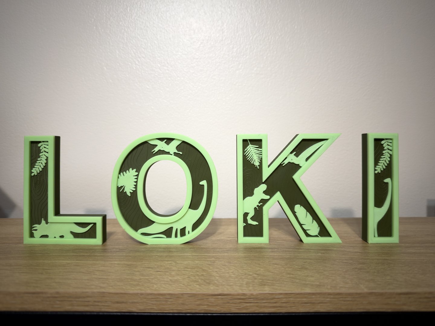 Free-standing 3D printed name letters with dinosaur silhouettes cut through a two-color face