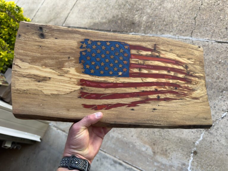 A hand holding the live-edge slab with the colored flag, outdoors.