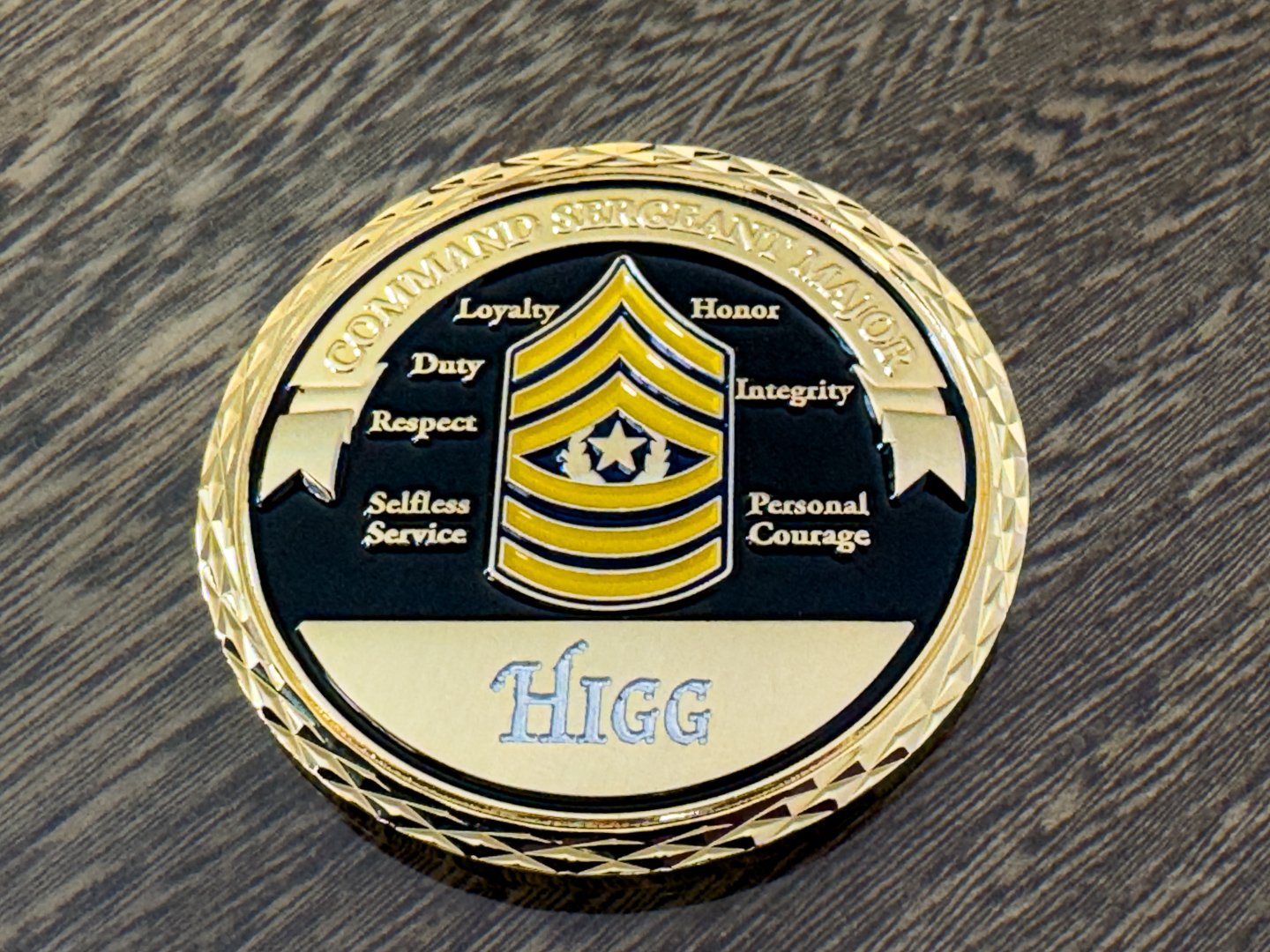 A command sergeant major challenge coin resting on a wooden display surface