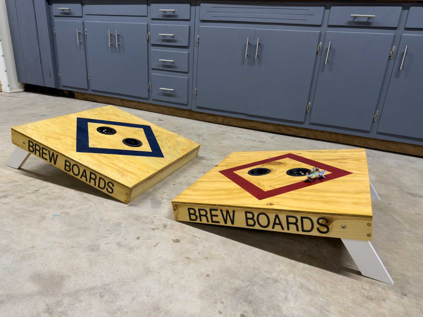 A pair of custom toss game boards in navy and red with a painted diamond target and lettered side rails