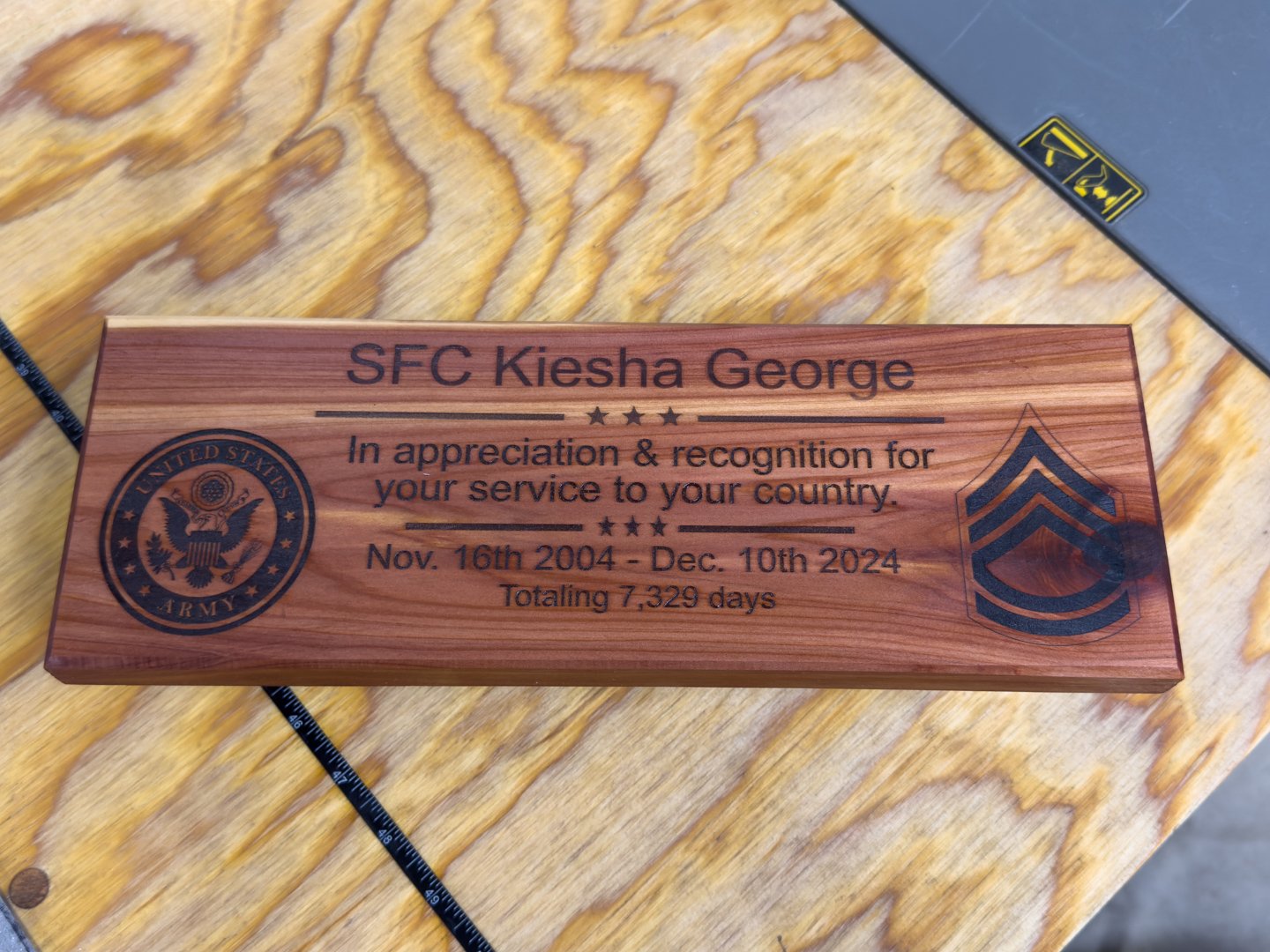 A wooden military service plaque with a laser-engraved name and service dates, set on a wooden surface