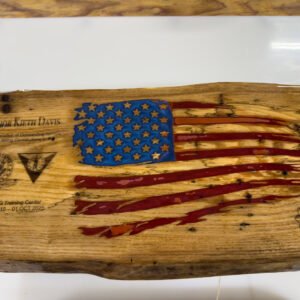 Live-edge wood slab with a tattered American flag in red and blue epoxy, natural wood stars, and engraved name
