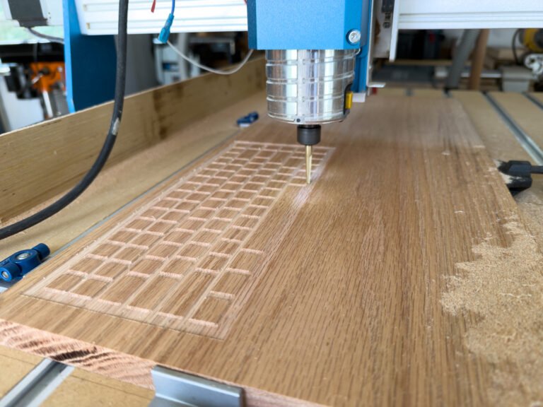 A CNC router cutting the keycap grid pattern into a solid wood panel on a workbench.