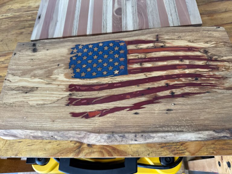 Tattered American flag live edge plaque on a workbench with its carved flag filled in blue and red