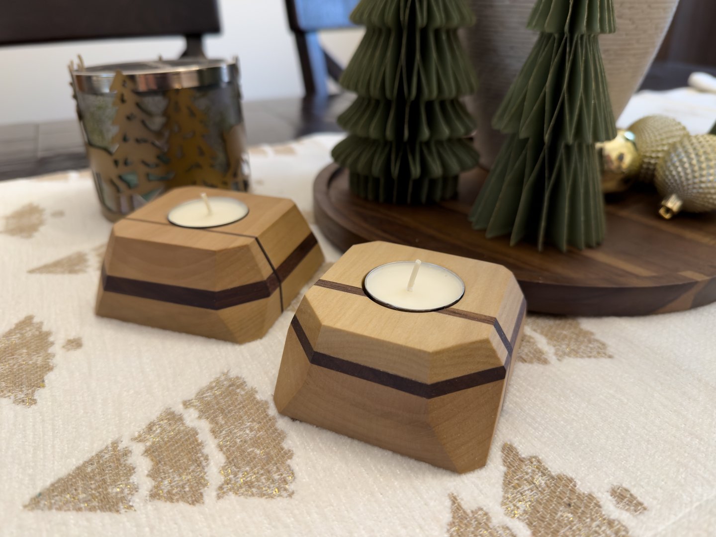 Faceted hardwood tea light holders with lit candles on a tabletop surrounded by holiday decor